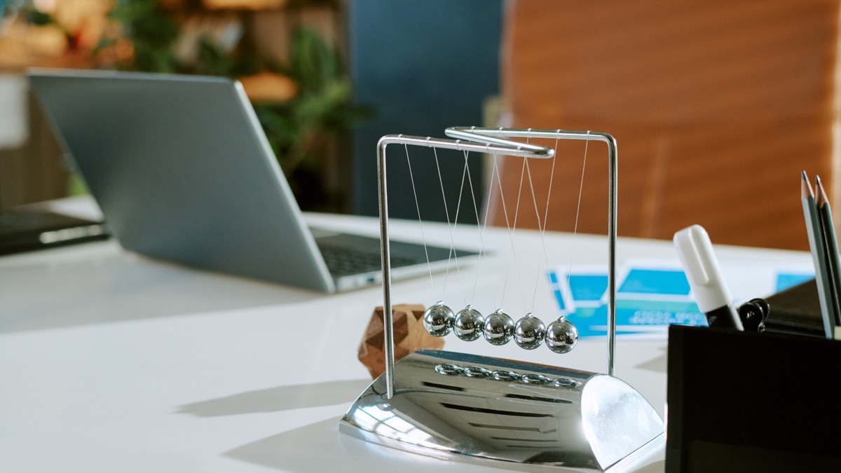 A chrome Newton's cradle mid-swing on a bright desk beside a laptop
