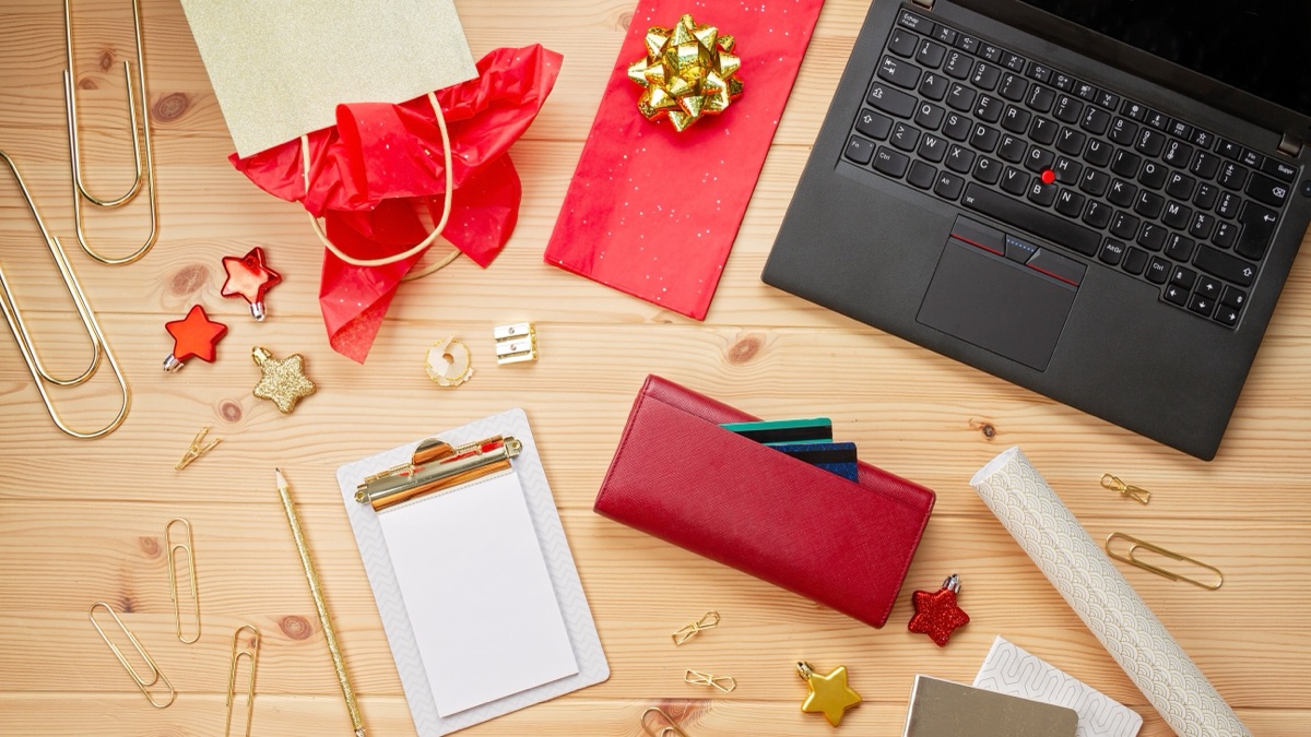 A laptop on a wooden desk beside kraft-wrapped gifts tied with ribbon