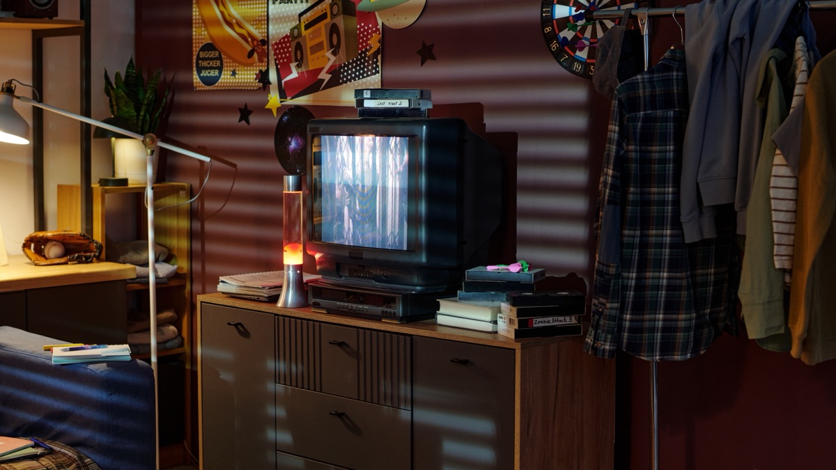 A retro computer corner with a beige monitor, lava lamp and cassette player in warm light
