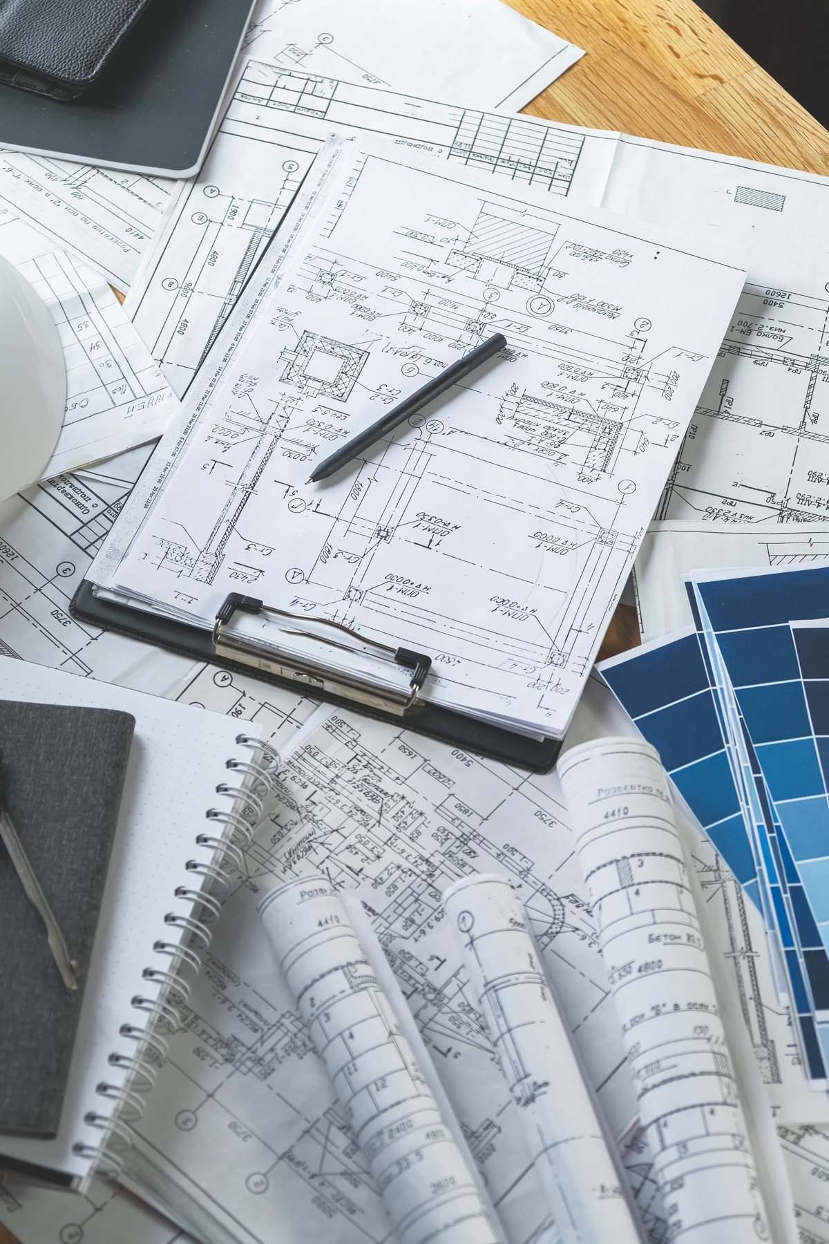 Architectural blueprints on clipboard with rolled technical drawings, color swatches, and material samples