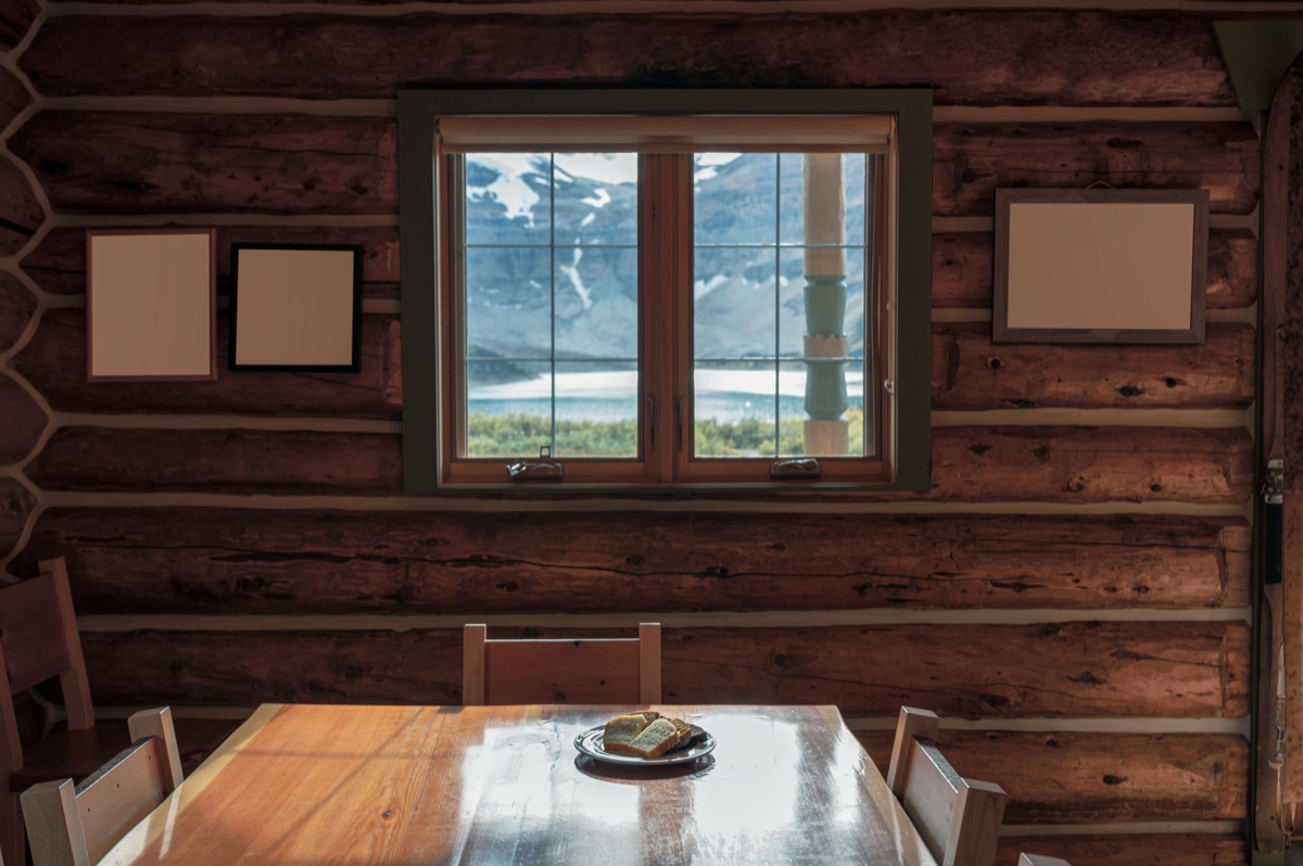 Wooden table against log cabin wall with window overlooking mountain landscape