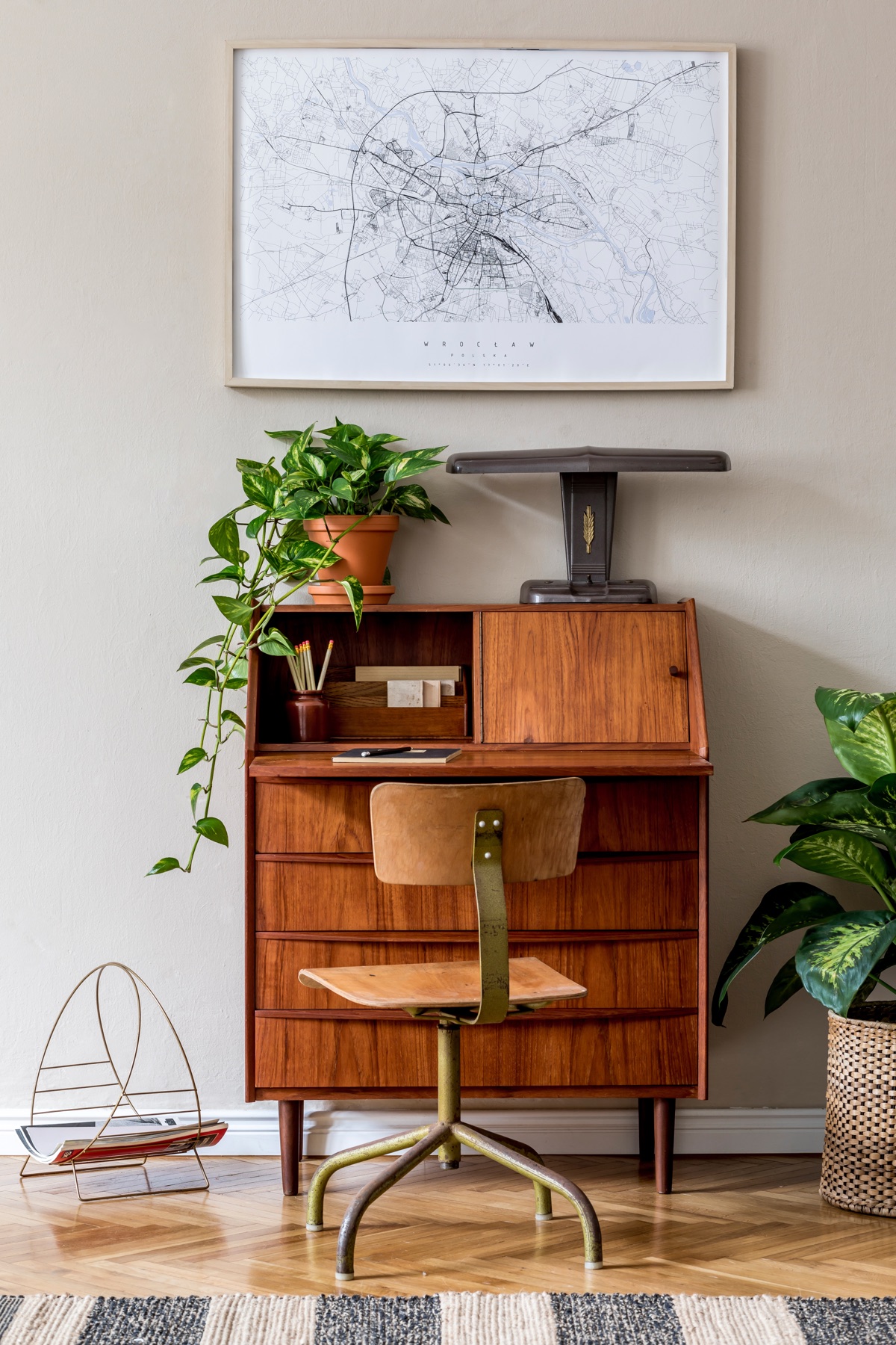Walnut mid-century secretary desk with brass swivel chair and potted plants against neutral wall